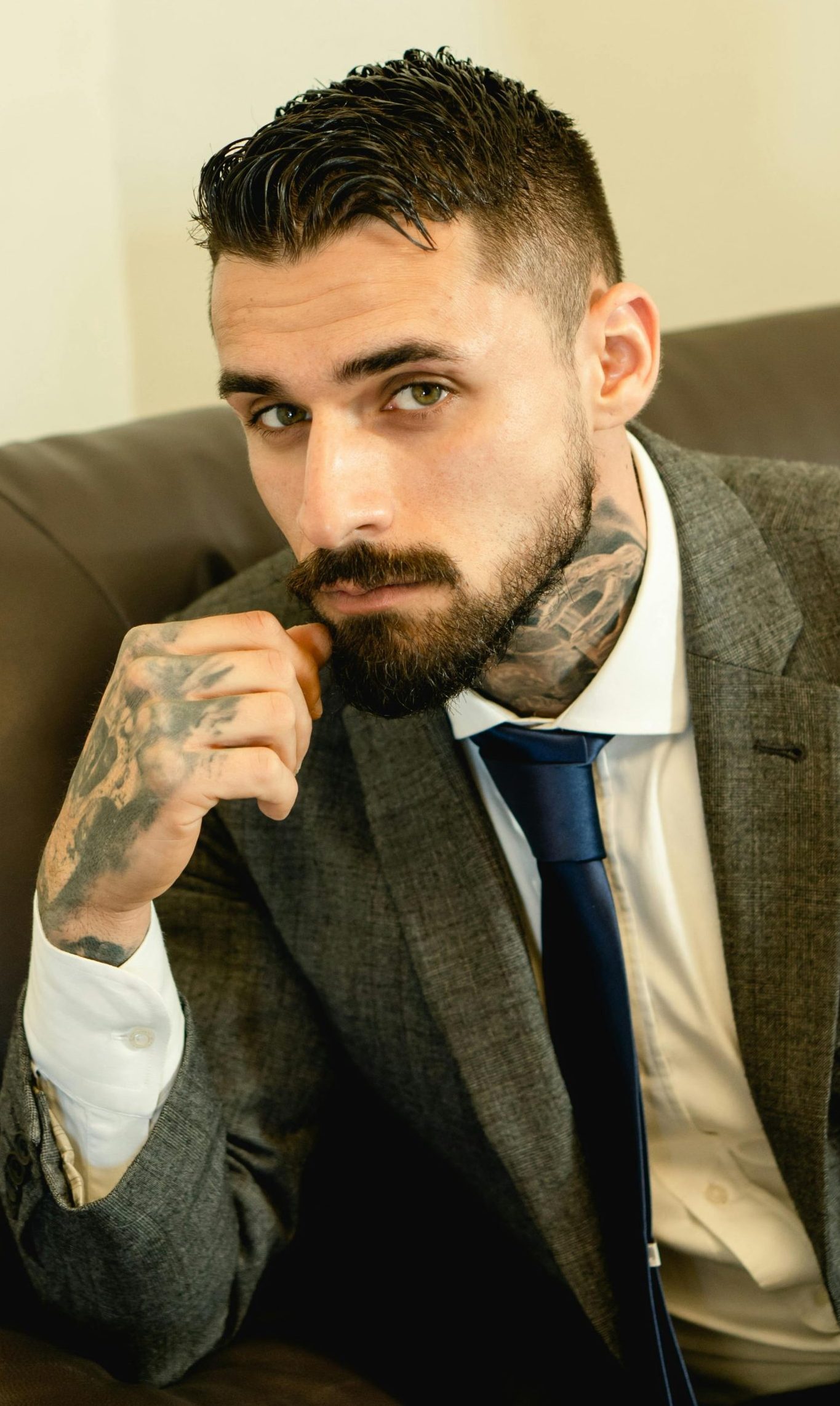 Elegant portrait of a bearded man with tattoos wearing a suit and tie.